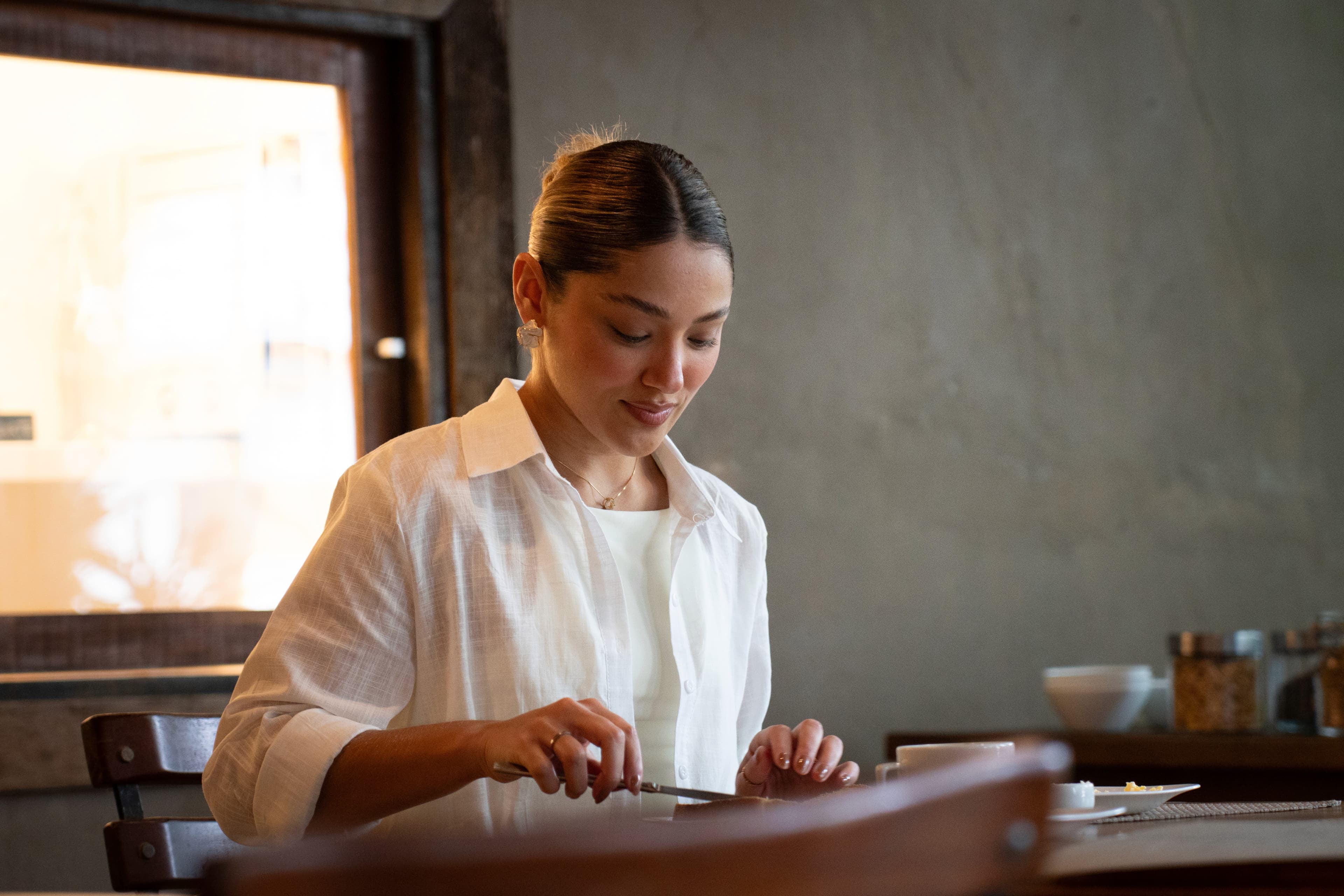 Hóspede de camisa branca à mesa do café da manhã em luz natural