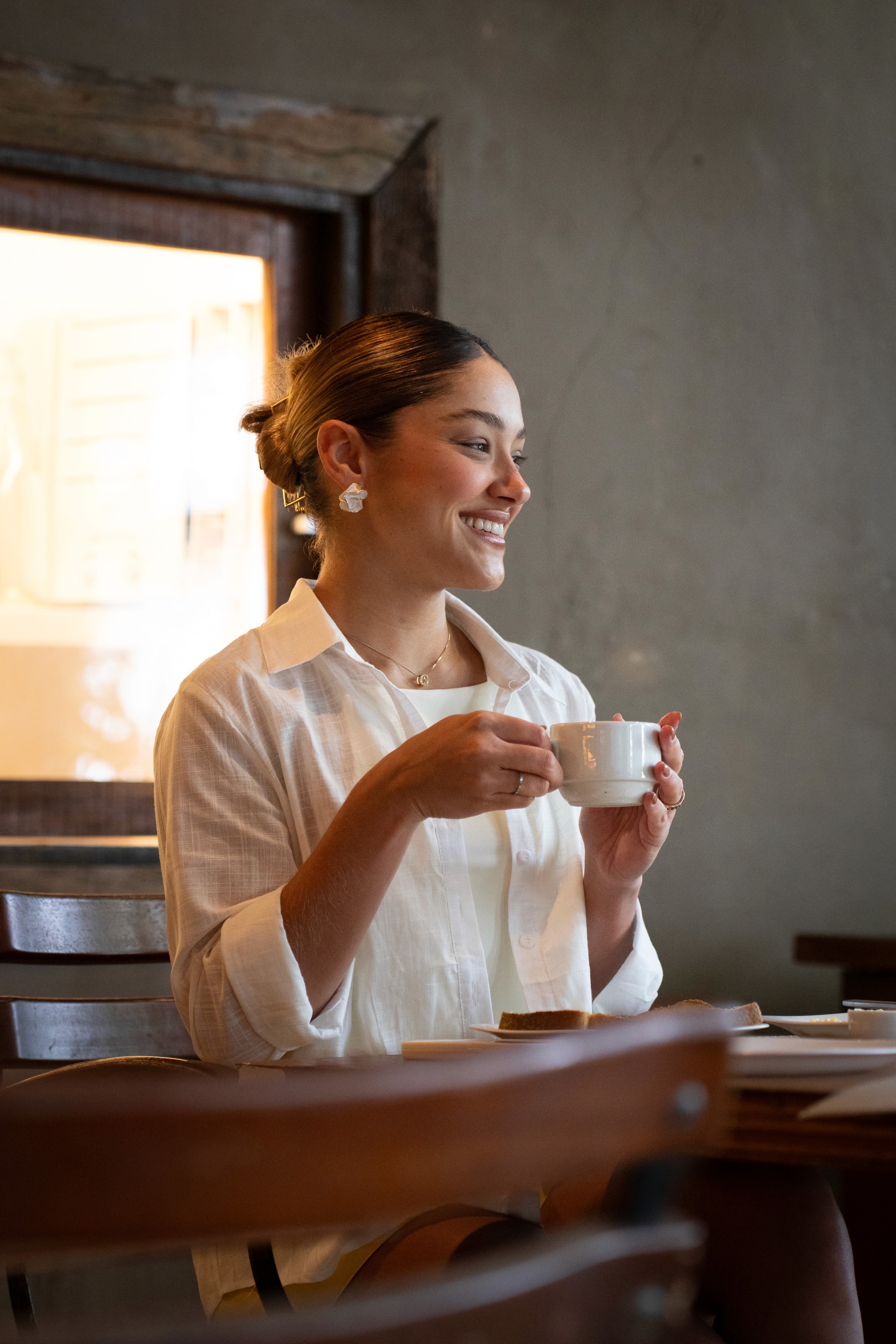 Hóspede sorrindo com xícara de café junto à janela