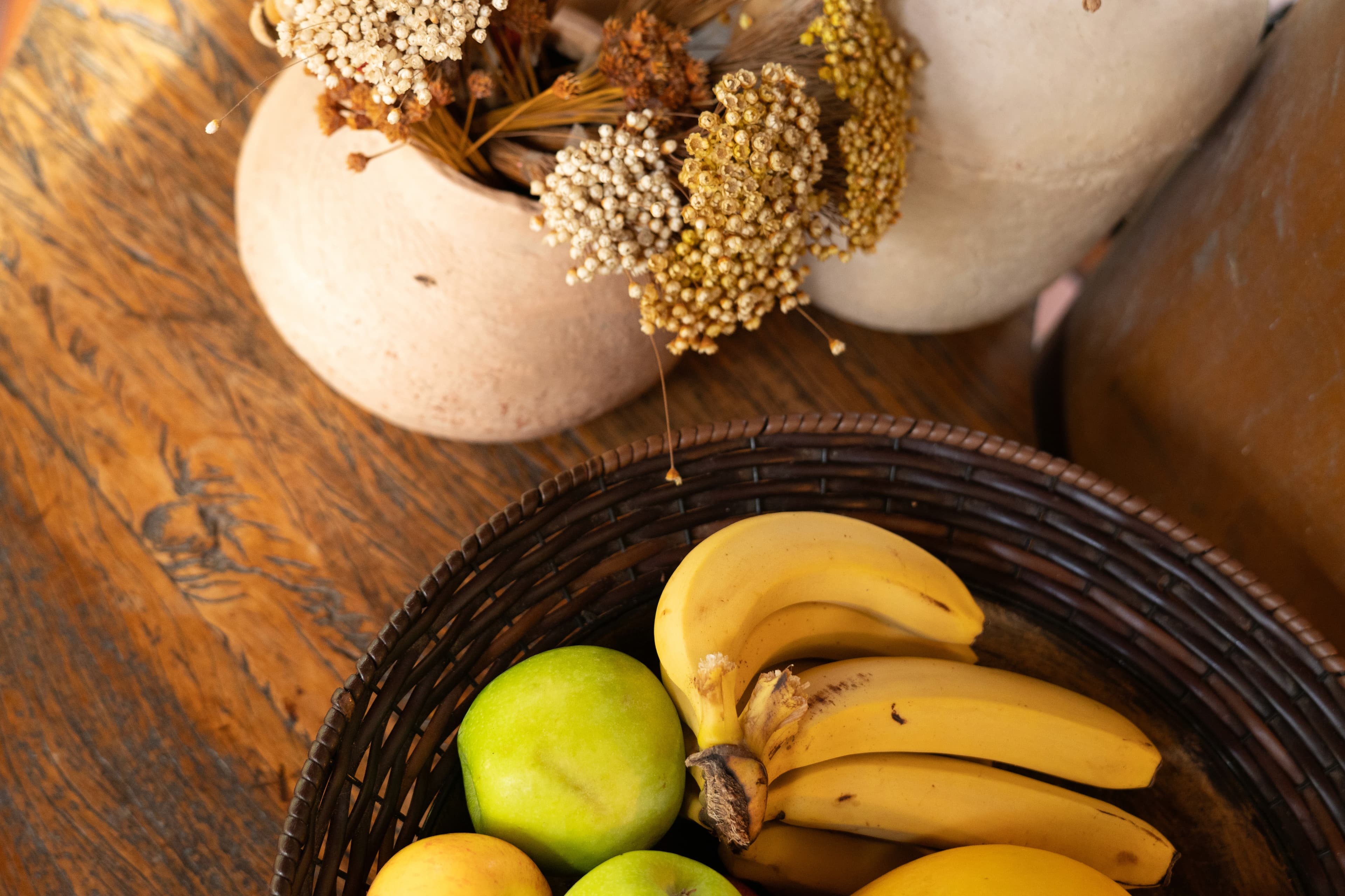 Cesto de frutas e arranjo de flores secas sobre mesa de madeira