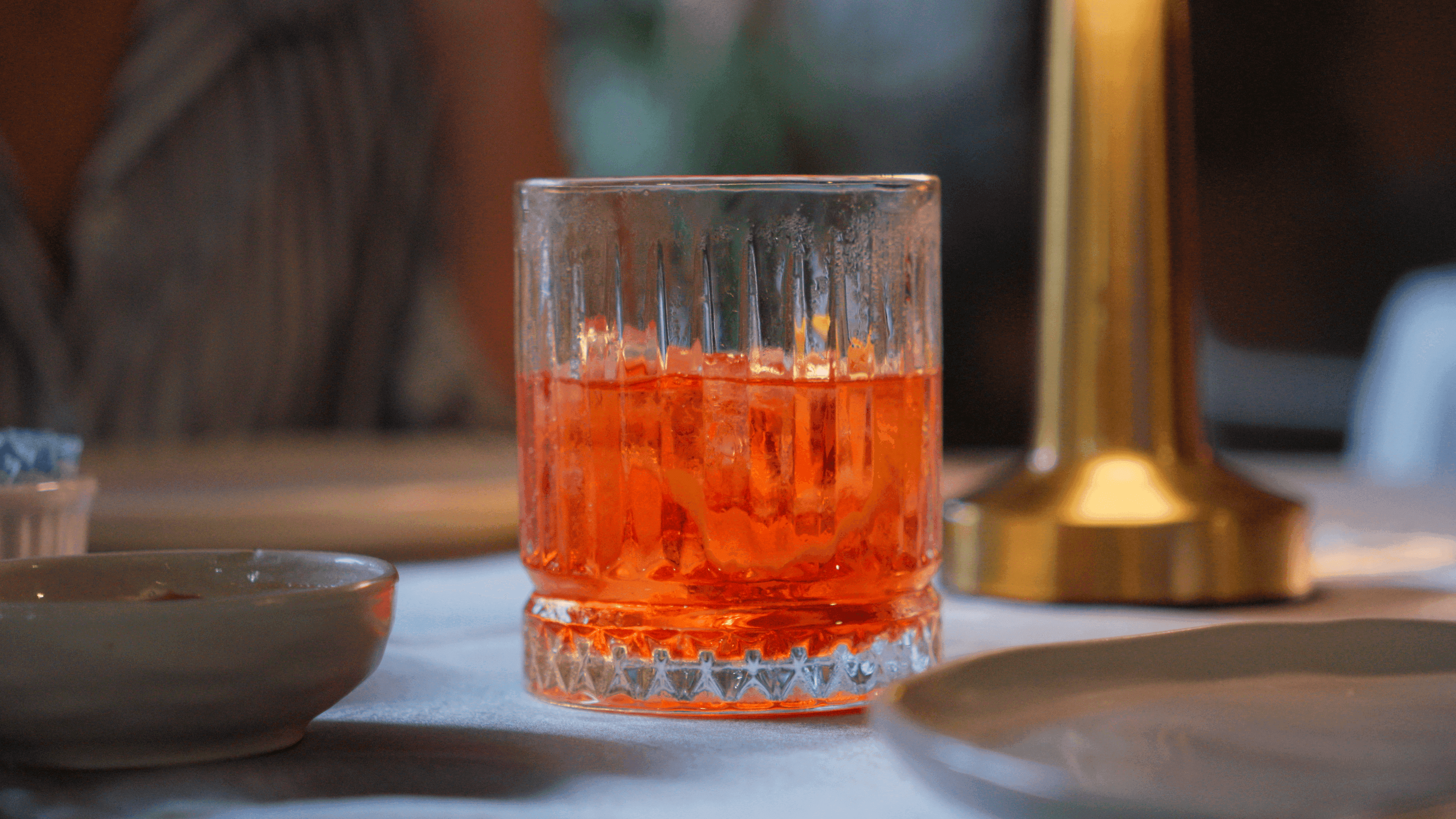Drink alaranjado em copo de vidro sobre a mesa posta do restaurante